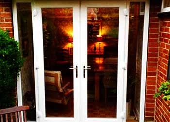 photo of double frnech doors from the outh side dimly lim from the inside finished in crisp white with floor to top glass panes and a just a very small but solid looking frame